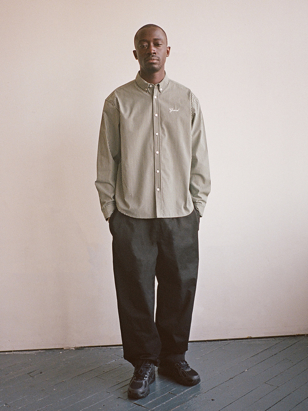 Man wearing a light-colored shirt and dark pants against a plain background